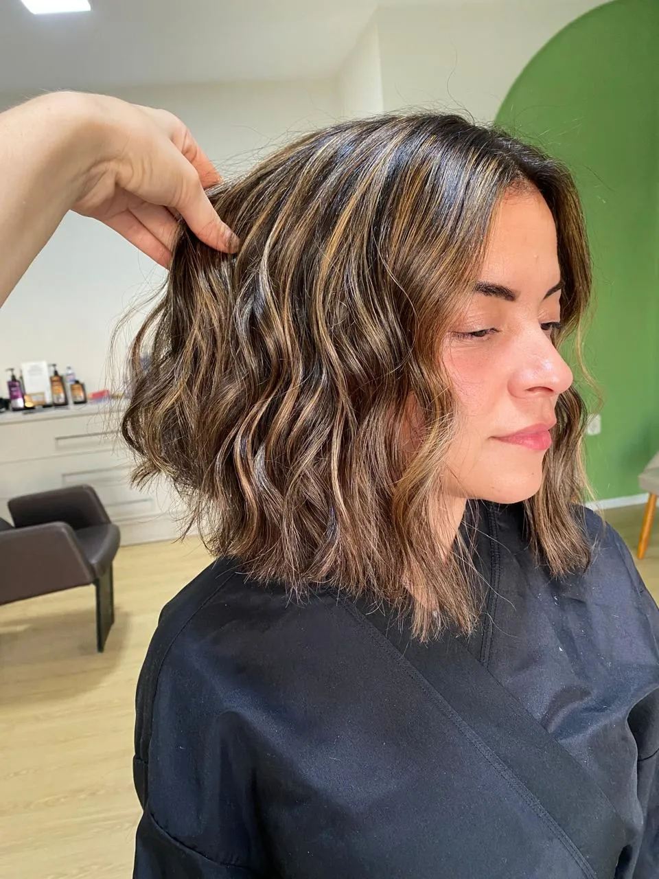 Cliente com cabelo na altura dos ombros, com ondas, sendo finalizada pela Lari no studio